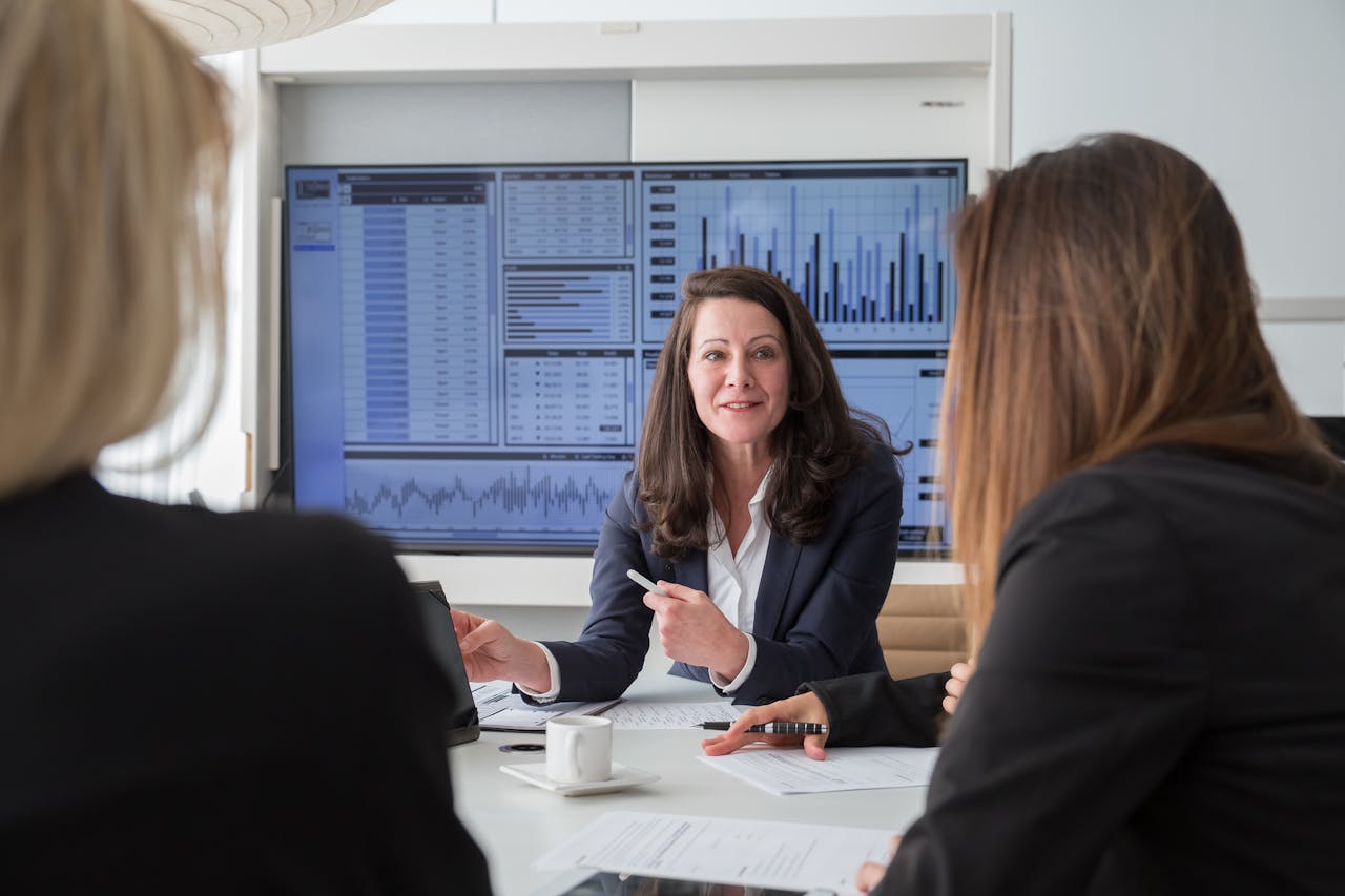 Professional businesswomen engaged in a meeting discussing data on a screen.