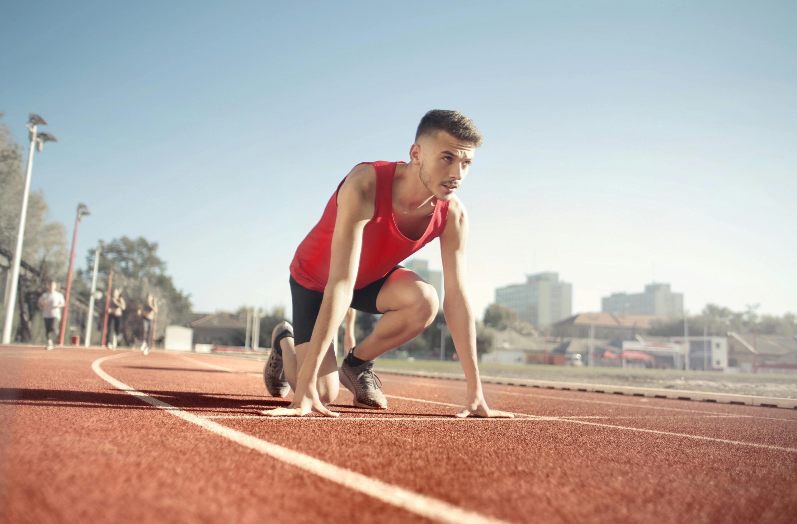 Young male athlete in start position on outdoor track, ready to sprint.